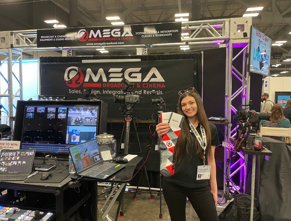 Person who works for Omega at trade show booth smiling and holding custom branded socks