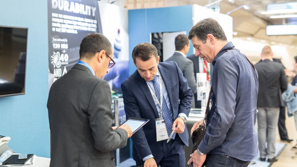 Thee businessmen at a tradeshow booth interacting with a new product