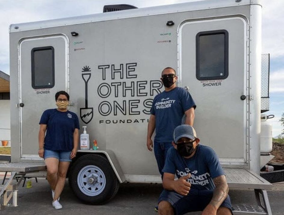 Three people in front of a mobile shower trailer.