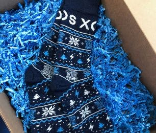 Custom branded holiday socks for Xos Trucks from Sock Club, featuring a blue winter themed design and blue crinkle paper in a box.