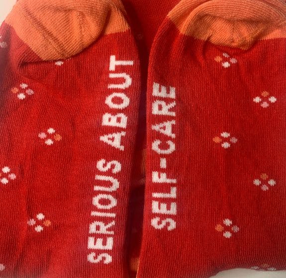 Red and orange custom socks with the message "serious about self-care" woven into the soles of the feet of the socks