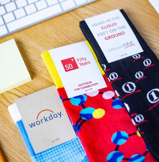 Custom socks on a desk showing the custom header card packaging for companies like Workday, Fifty Years, Head In The Cloud Feet On The Ground
