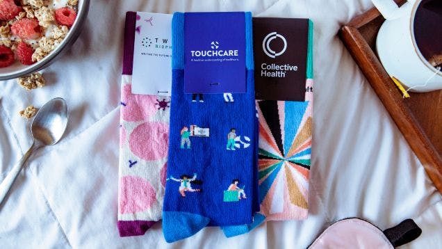 Custom socks for Touchcare, Collective Health, and Twist Biosciences laying on a hotel bed at a sales conference