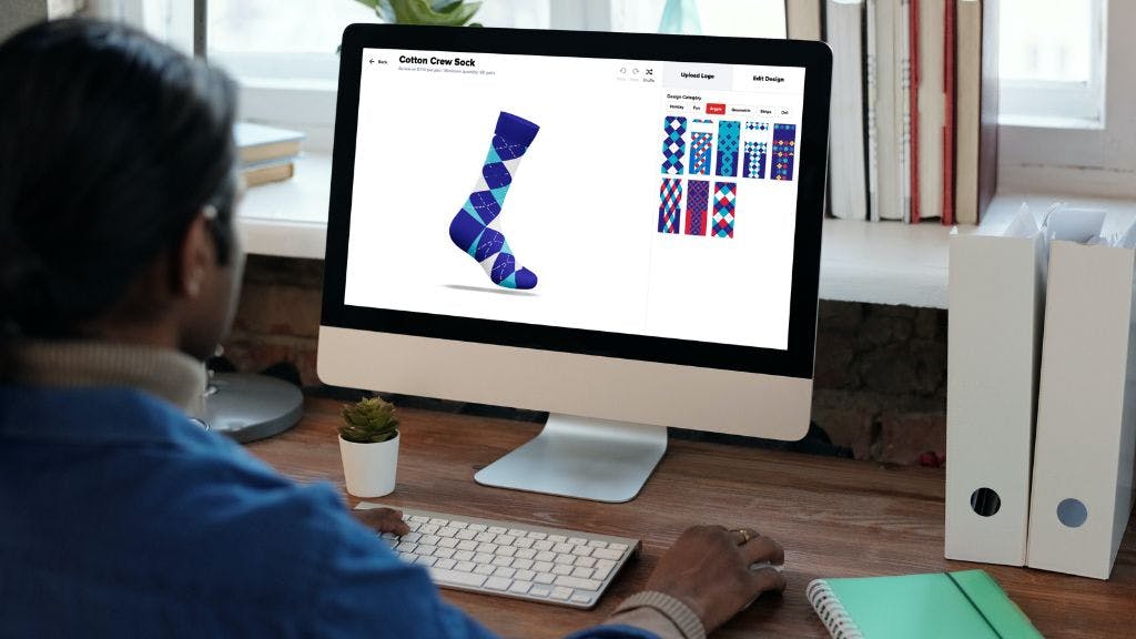 Man designing custom socks through Sock Club's online custom sock designer in his home office on a design with books and plants