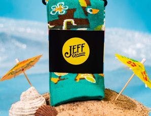 A beach-themed sock sitting in a pile of sand with umbrellas and shells on a blue background