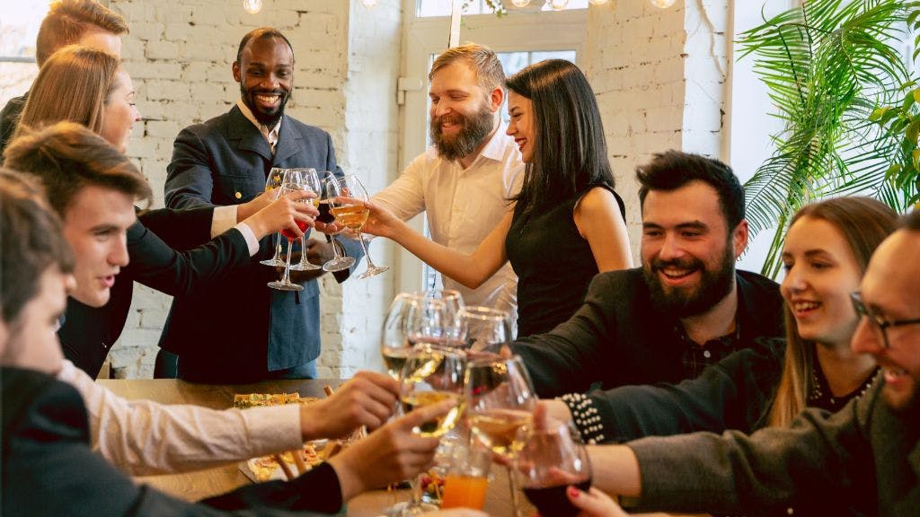 A group of co-workers at a company holiday party in their modern office cheersing with their wine glasses