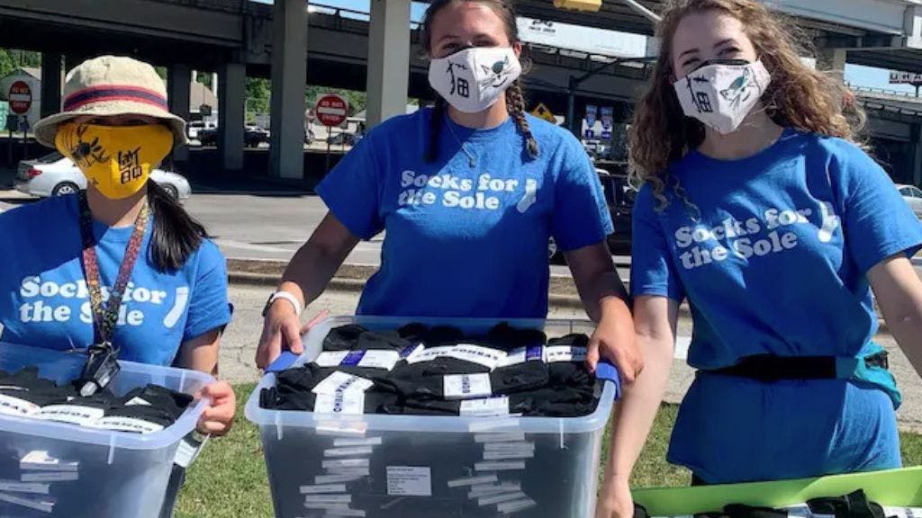 Volunteers in blue t-shirts in masks holding bins of custom socks that Sock Club has donated to their organization