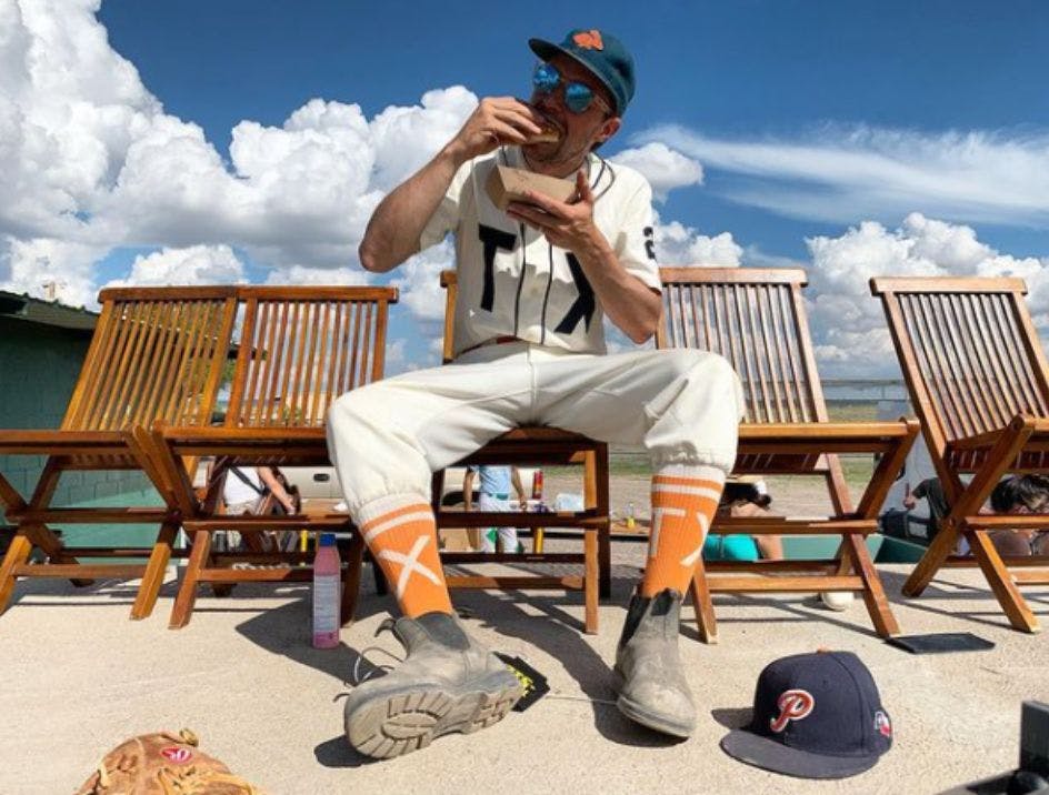 Baseball player wearing custom team socks featuring his team's logo, eating a hot dog outside