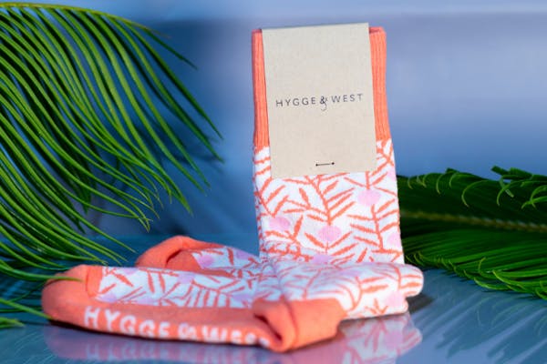 custom socks with logo of hygee and west in orange against tropical palm leaf backdrop
