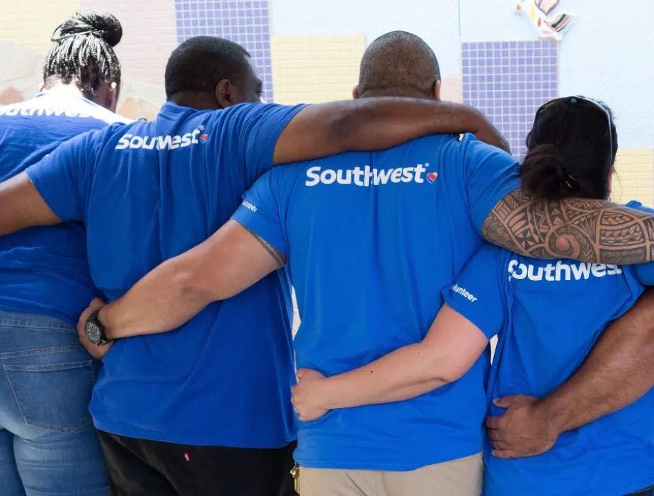 Southwest employees in blue t-shirts showcasing the brand's logo with their arms around each other shot from behind