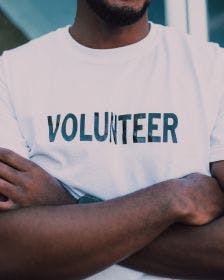 Young volunteer with his arms crossed wearing a white t-shirt that says "Volunteer" on it in black letters