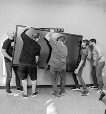 Alcuni membri del team SoCreate stanno sollevando un display touch per sala conferenze da 300 libbre. Questo era uno dei tanti poiché li abbiamo in ogni stanza del quartier generale di SoCreate.