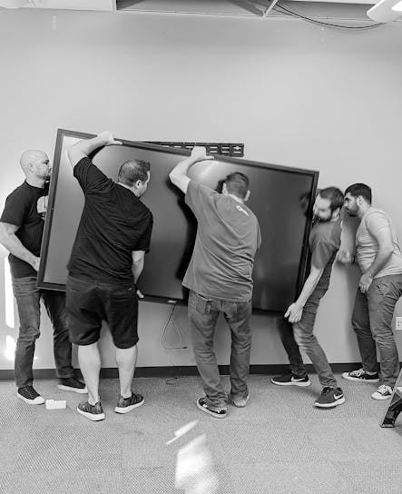 Einige Mitglieder des SoCreate-Teams heben bei ein 130 Kilo schweres Touch-Display für den Konferenzraum hoch. Das war eines von vielen, da wir in jedem Raum des Hauptsitzes von SoCreate eines haben.