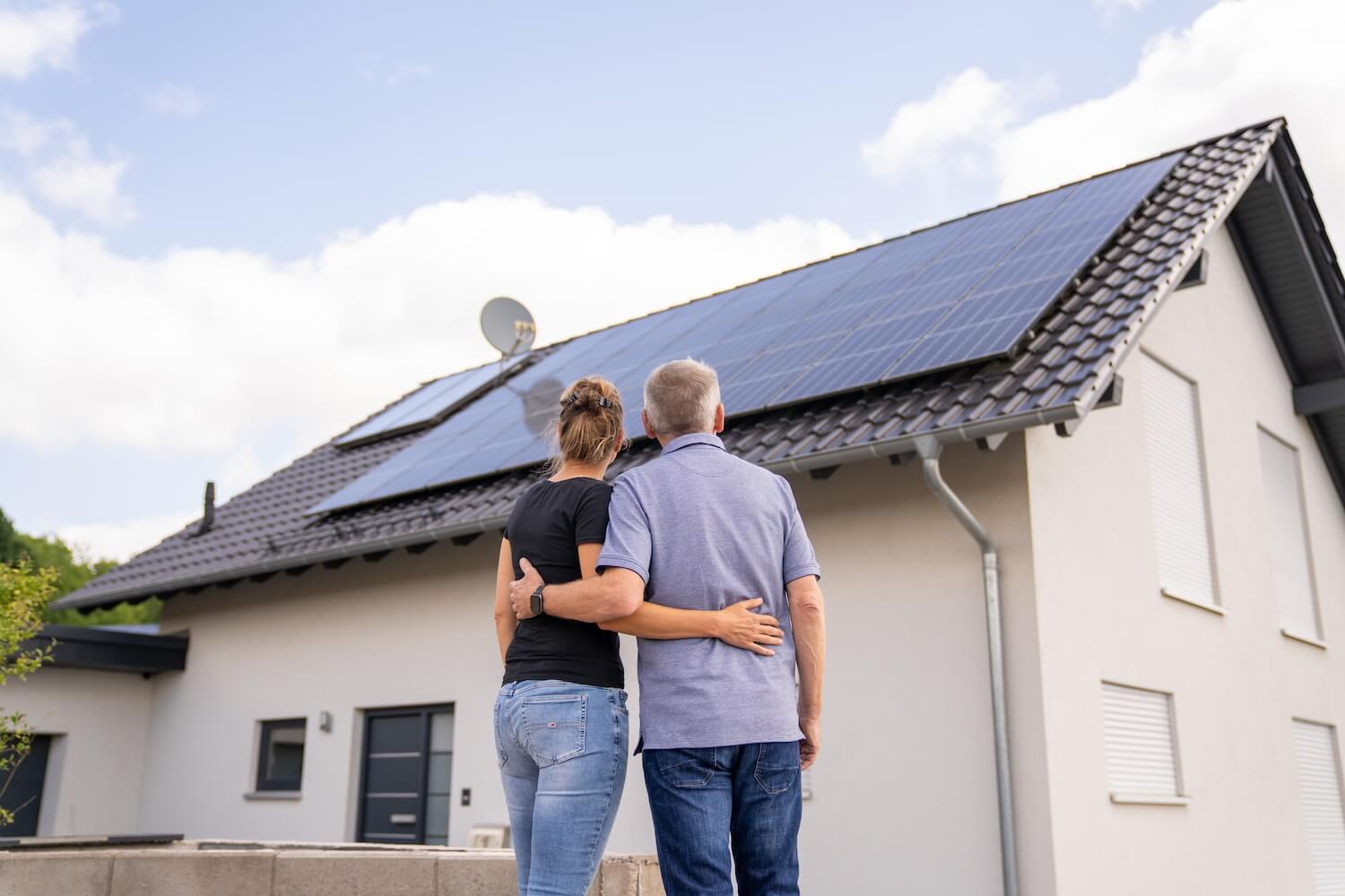 Paar steht mit dem Rücken zur Kamera und schaut auf eine Solaranlage auf dem Hausdach