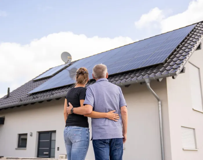 Paar steht mit dem Rücken zur Kamera und schaut auf eine Solaranlage auf dem Hausdach Paar steht mit dem Rücken zur Kamera und schaut auf eine Solaranlage auf dem Hausdach