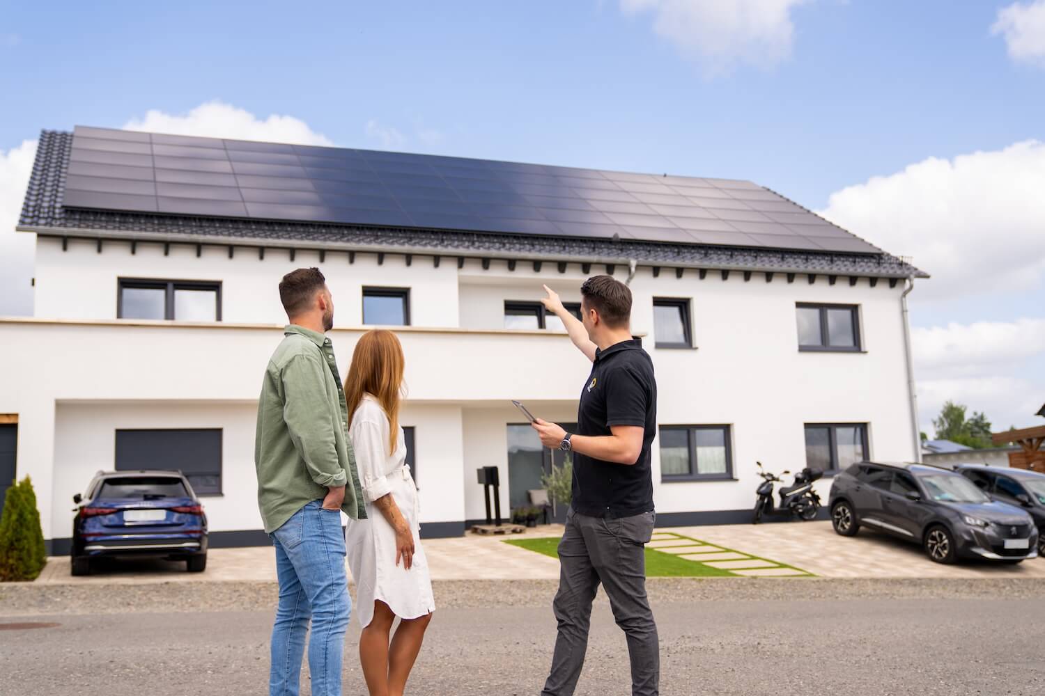 Paar und Photovoltaik Berater stehen vor Mehrfamilienhaus mit Solaranlage und unterhalten sich