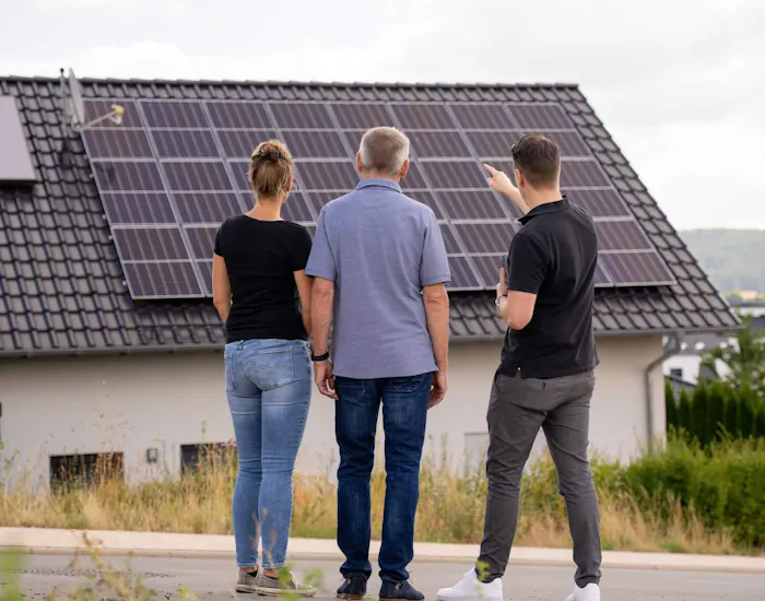 Paar und Solarberater stehen vor einem Wohnhaus und schauen auf die Solaranlage auf dem Dach Paar und Solarberater stehen vor einem Wohnhaus und schauen auf die Solaranlage auf dem Dach
