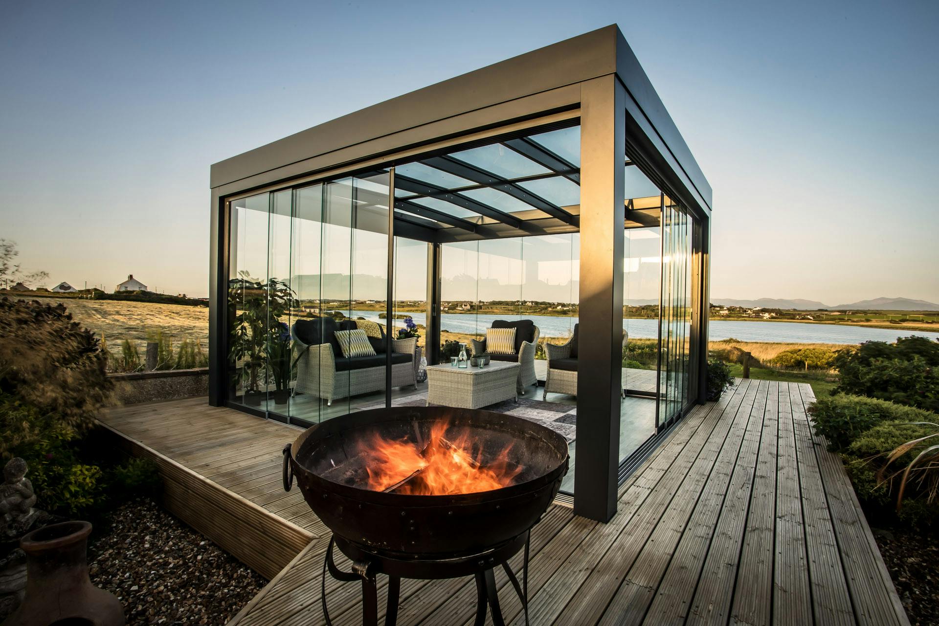 burning fire pit on summer evening with modern cube glass room in background