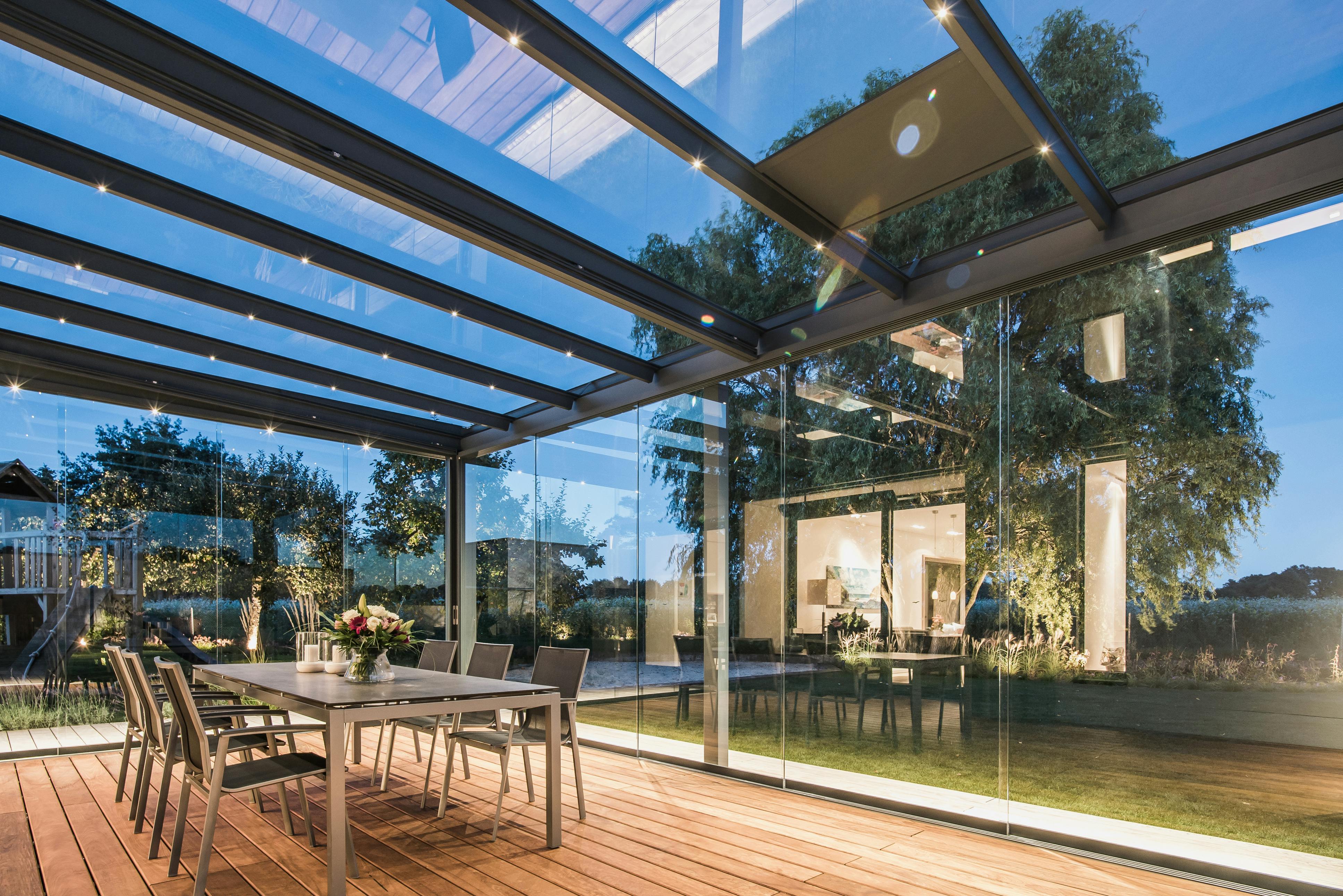 Glass room at night time with views out to the garden and a dining table and chairs inside
