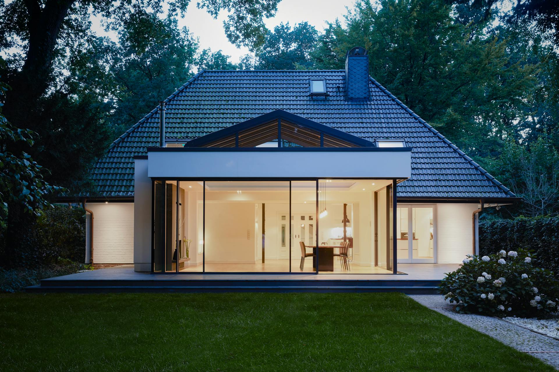 Illuminated detached home with glass room at dusk