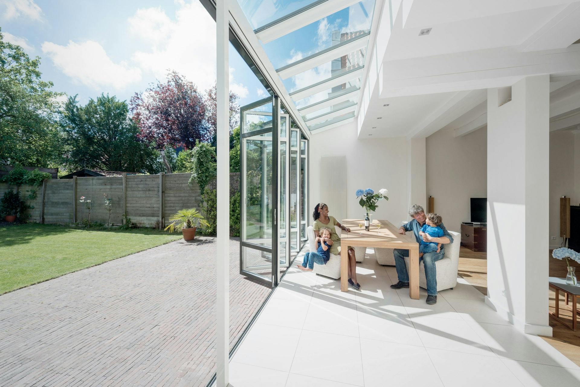Family relaxing in bright and airy white home extension with open glass doors