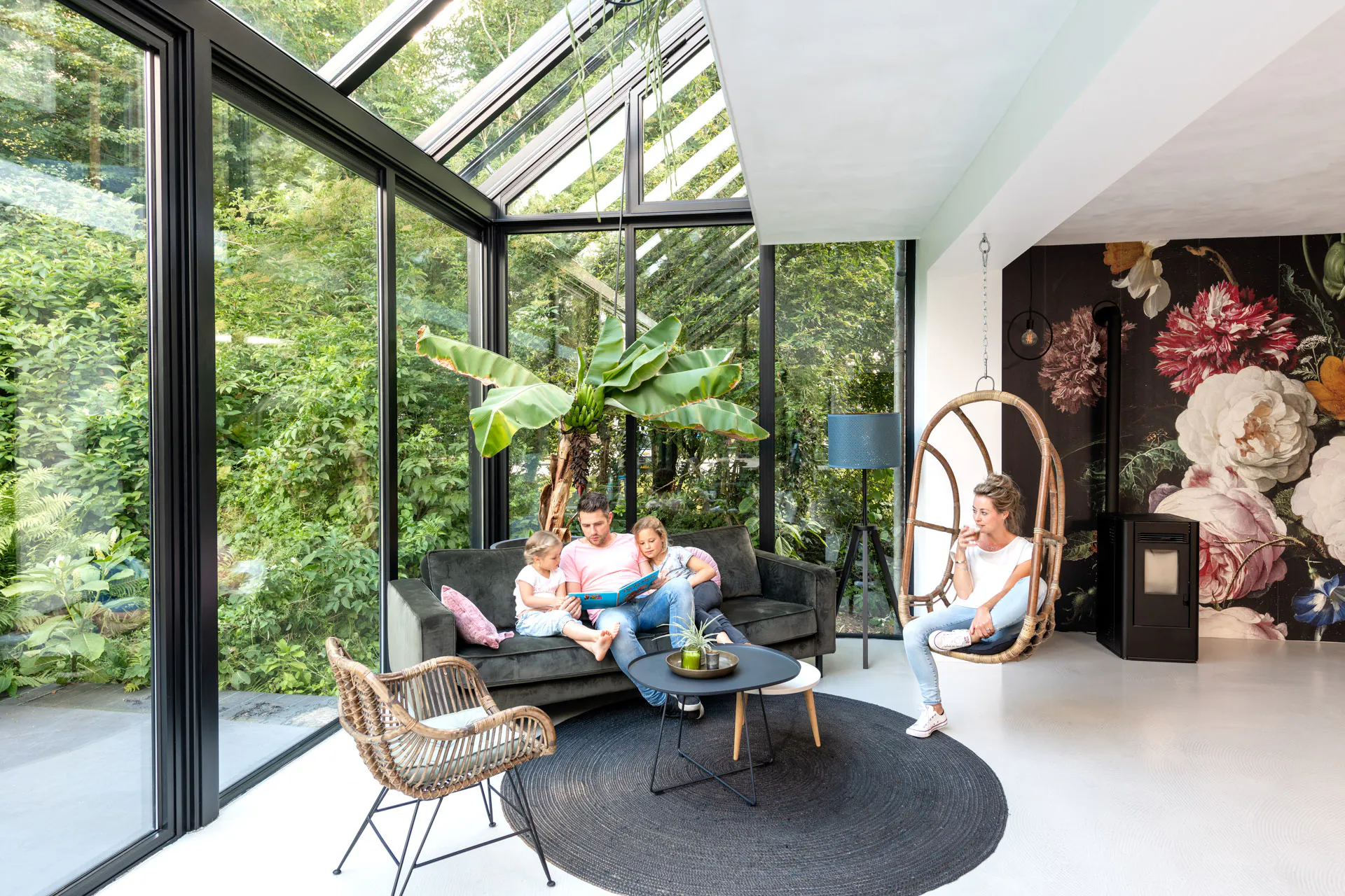 a wintergarden glass extension used as a living room with a family man and two young girls relaxing on a sofa