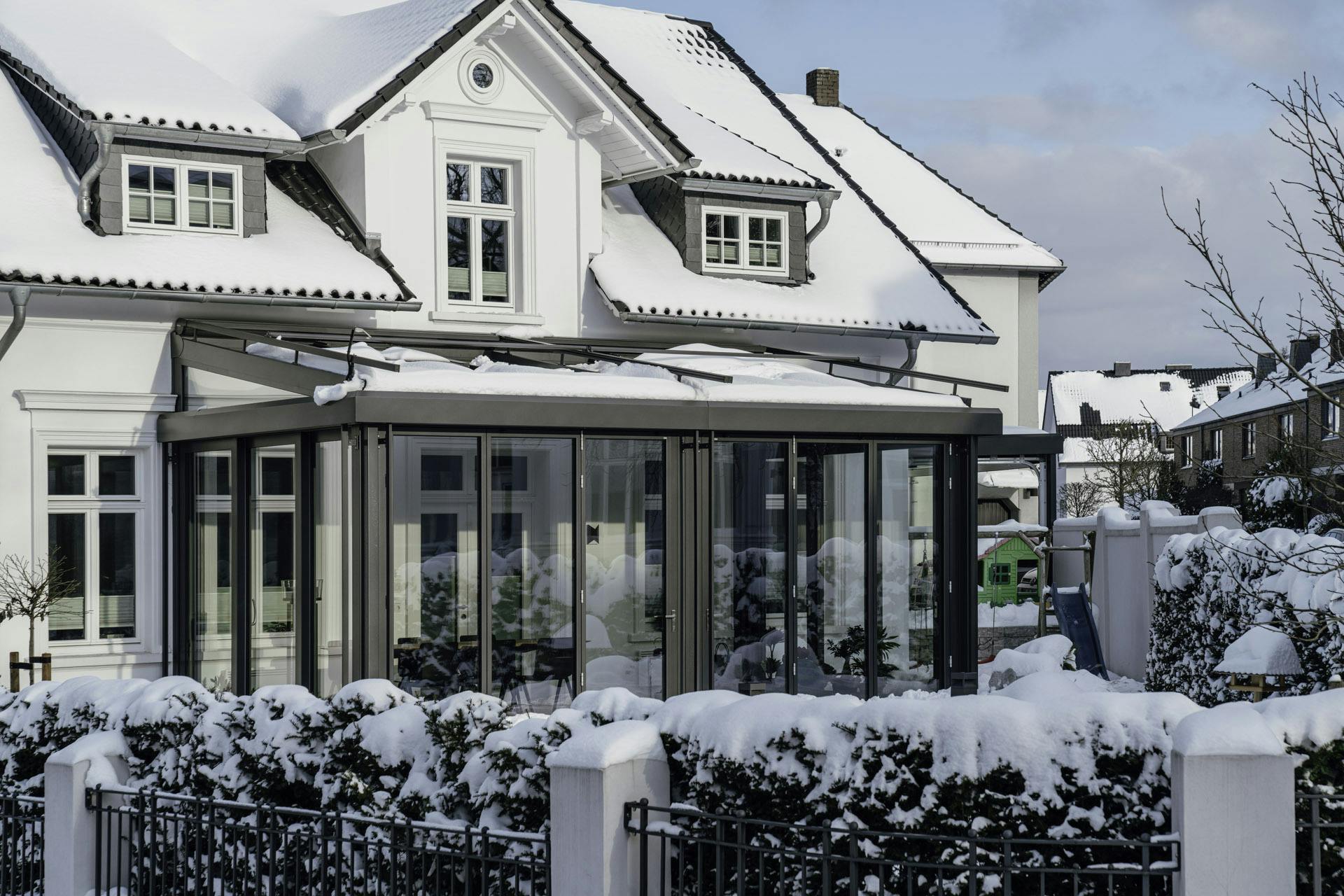 glass home extension on large white detached house in winter snow