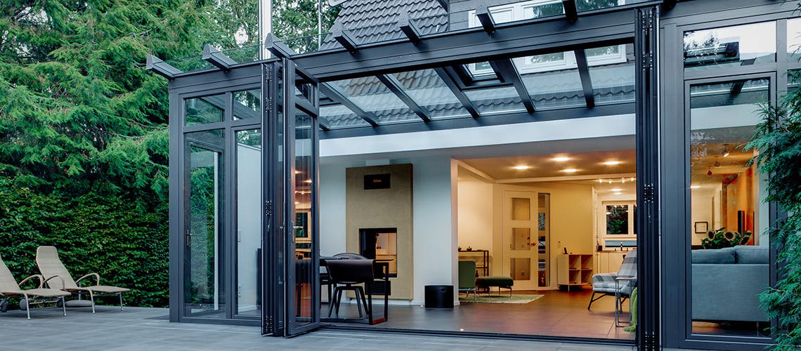 A house with a glass and aluminium extension at the side and two sun loungers on the patio