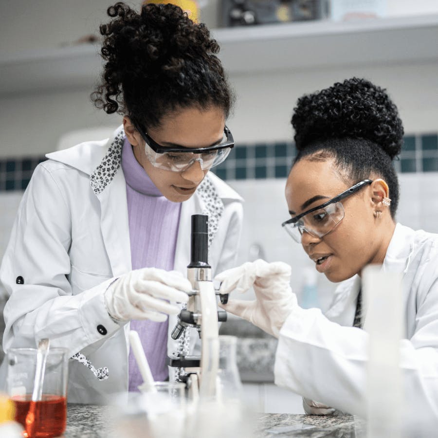 Doutoras negras analisando amostra de material em lâmina de miscroscópio