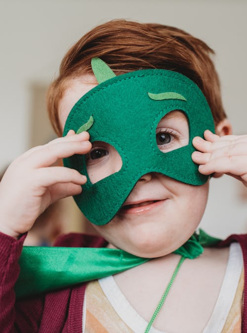 little boy is wearing a green costume mask