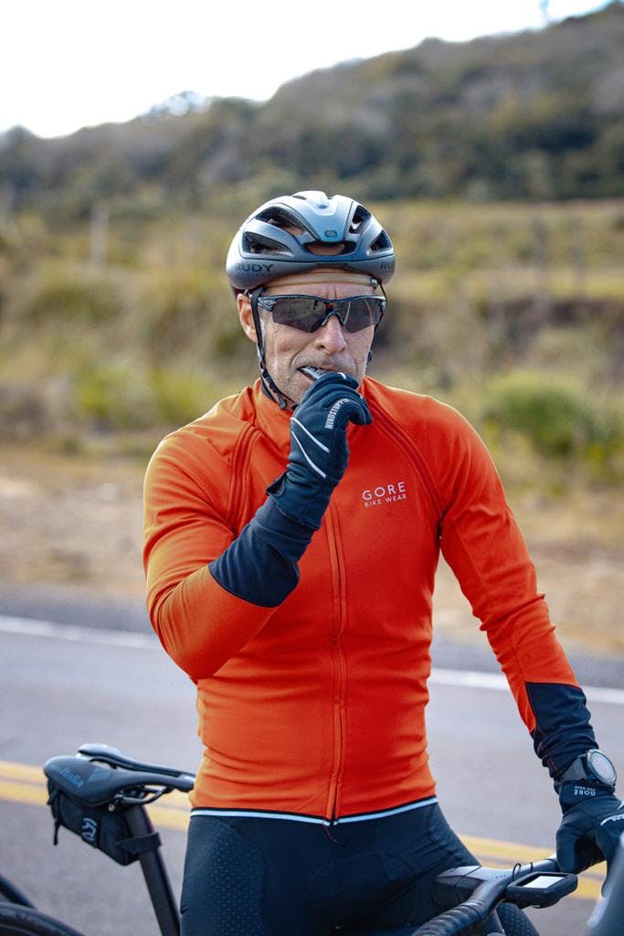 Homem ciclista sentado na bike à beira da estrada tomando gel de carboidrato