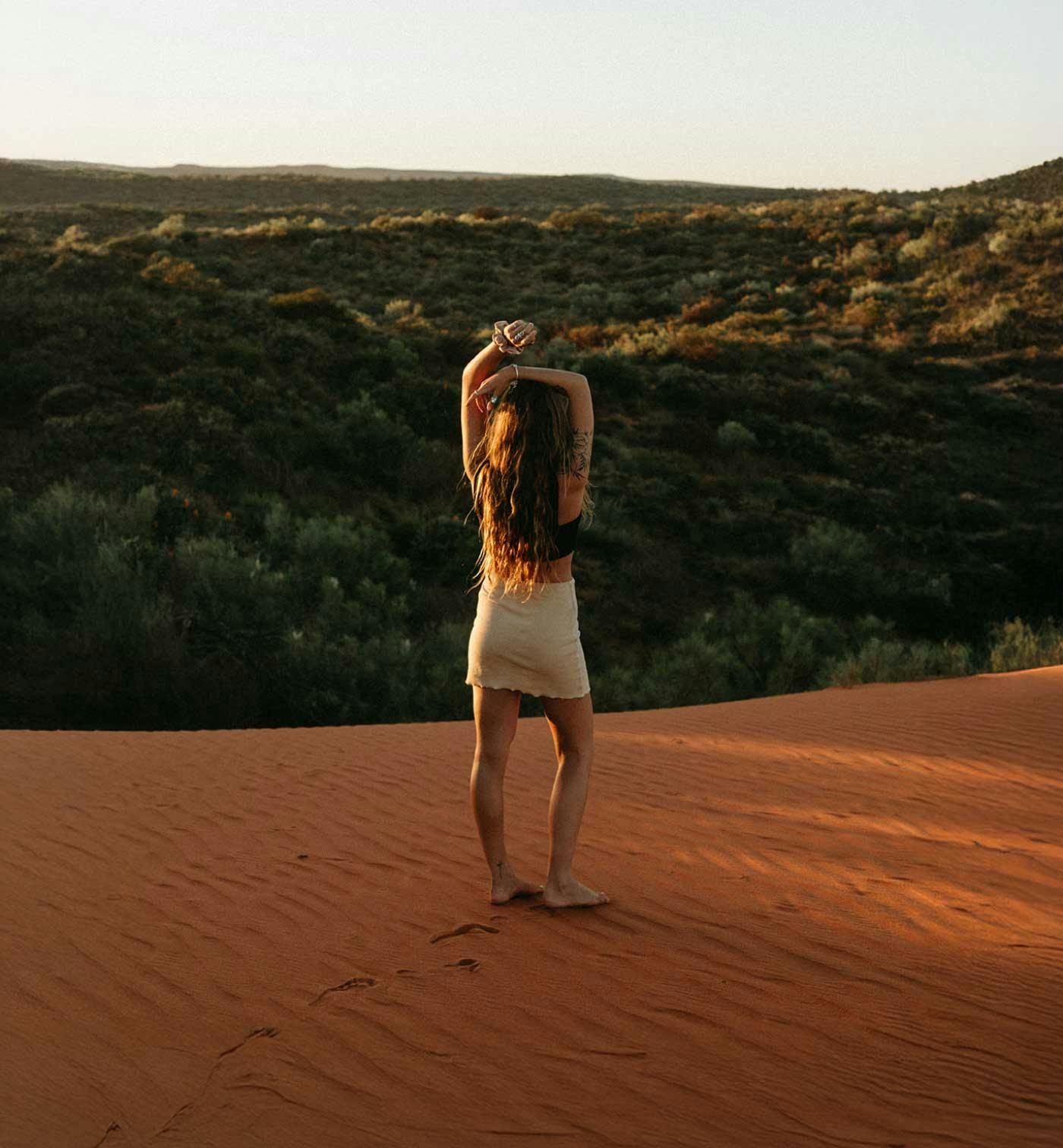 woman standing on sand dune facing endless views of greenery