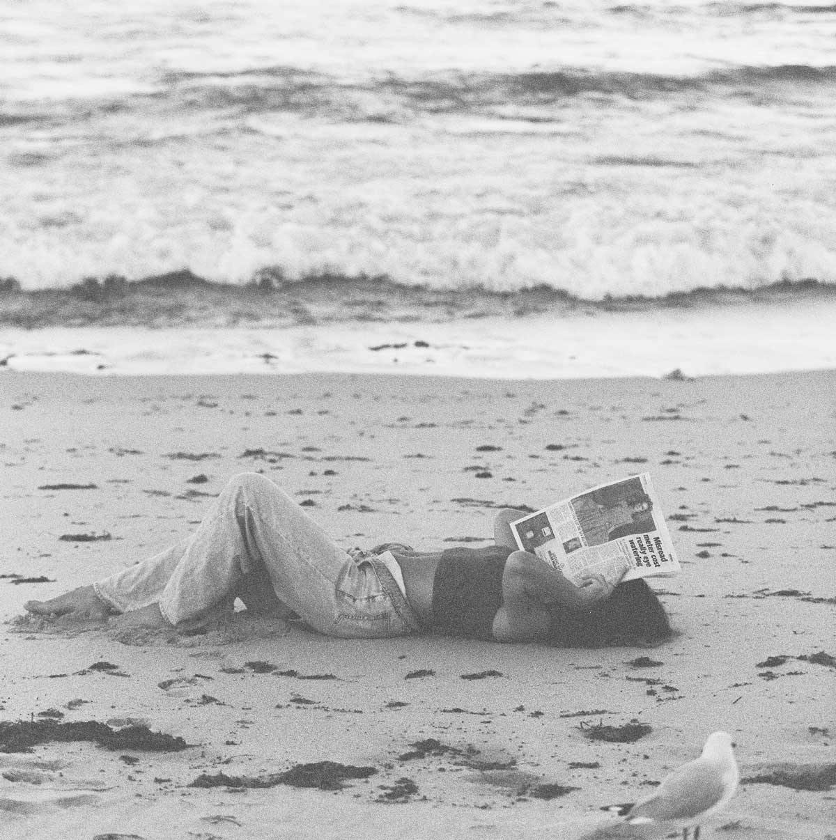 a woman laying on sand holding a magazine