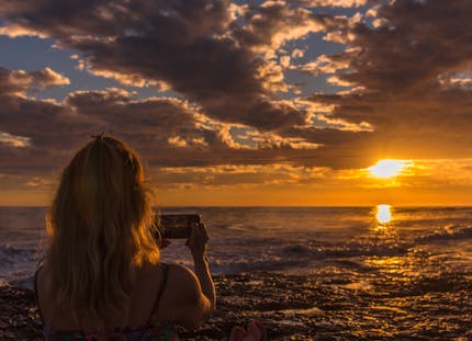 Women taking a photo of a sunset at the beach