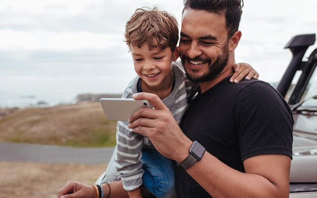 Man holding his son and looking at a mobile phone