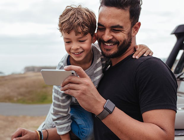 Man holding his son and looking at a mobile phone