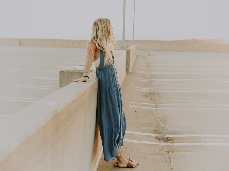 Frau in blauem Kleid lehnt an Mauer.