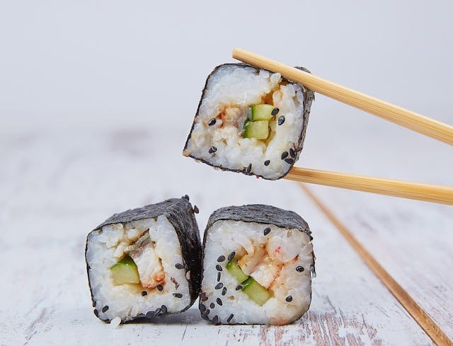 Asian Food Lovers GDE Drei Rollen Sushi, die mit Stäbchen gegessen werden