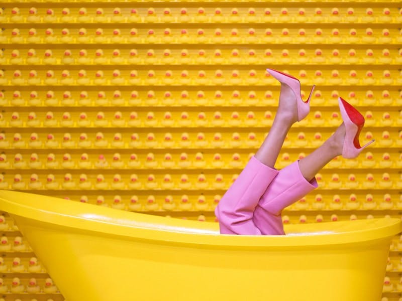 Frauenbeine mit rosaroten Pumps gucken aus gelber Badewanne hervor