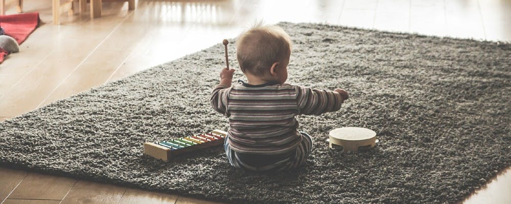 Ein Kleinkind sitzt auf einem Teppich und spielt mit Musikintrumenten.