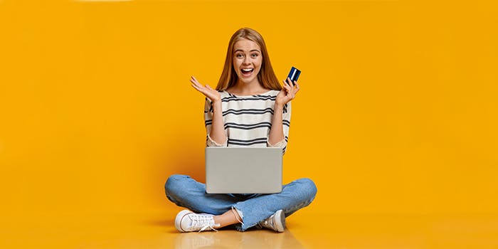 Singles' Day - Die besten Gutscheine und Angebote Frau sitzt vorm Laptop mit Kreditkarte und freut sich über den Einkauf