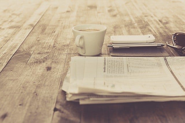Zeitung neben Kaffeetasse und Handy auf Holztisch