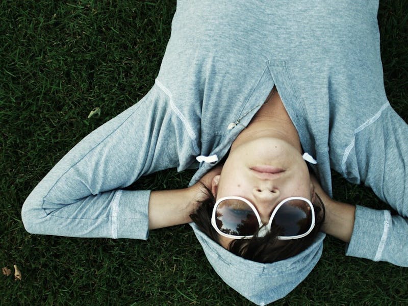 Ein Mann mit grauem Hoodie und Sonnenbrille liegt auf dem Gras.