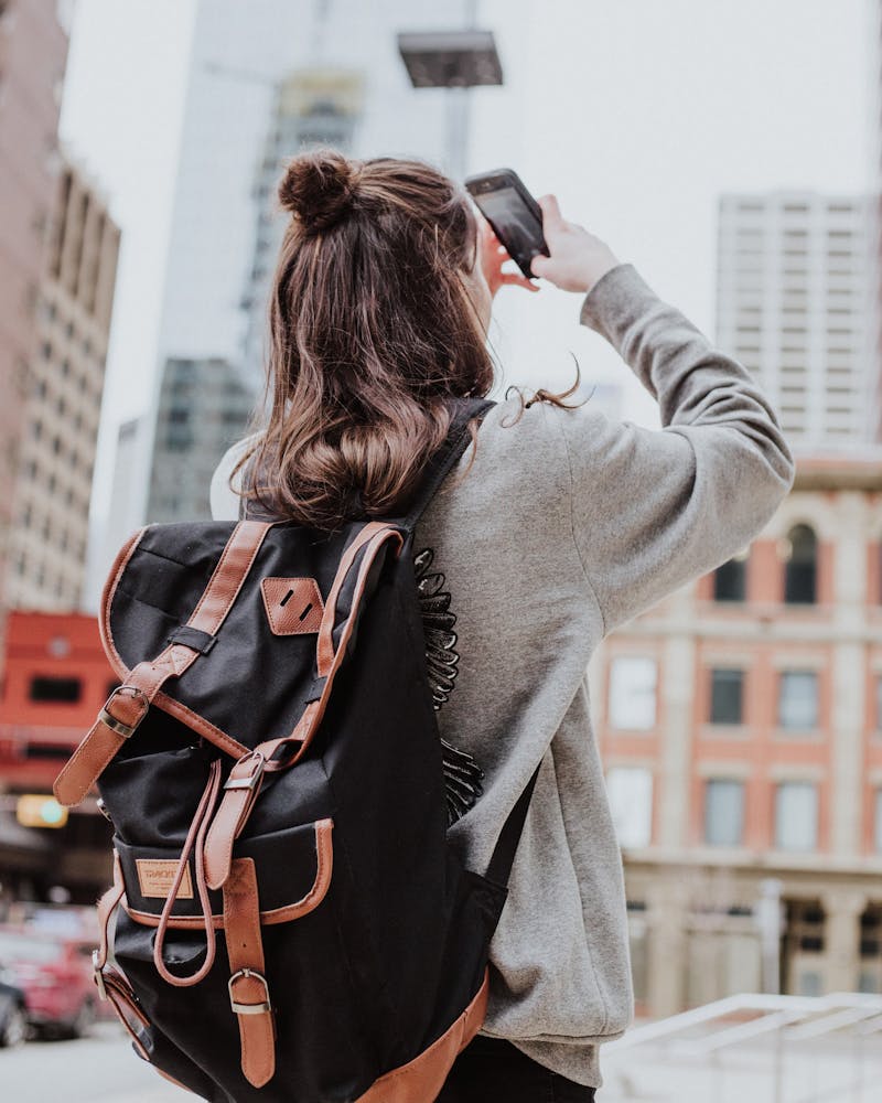 Frau mit Rucksack fotografiert in Großstadt mit Smartphone