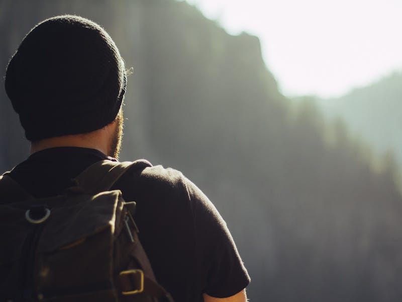 Ein Mann mit Mütze blickt in die Ferne, im Hintergrund ein Wald.