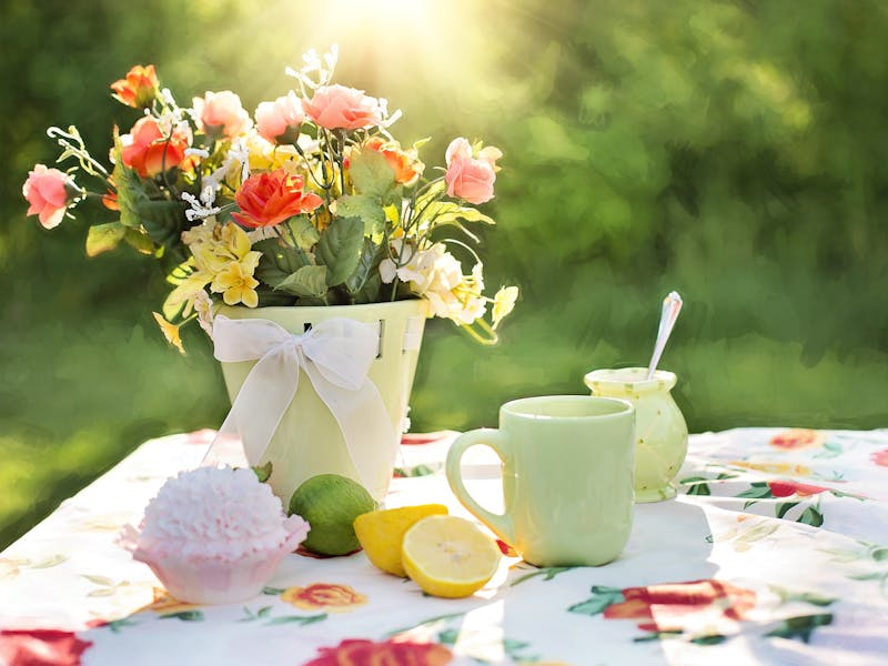 Ein Gartentisch mit Blumentischdecke und Blumen in einer Vase.