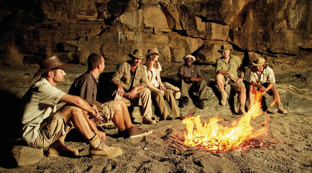 Gruppe Männer und Frauen in Outdoor-Kleidung am Lagerfeuer