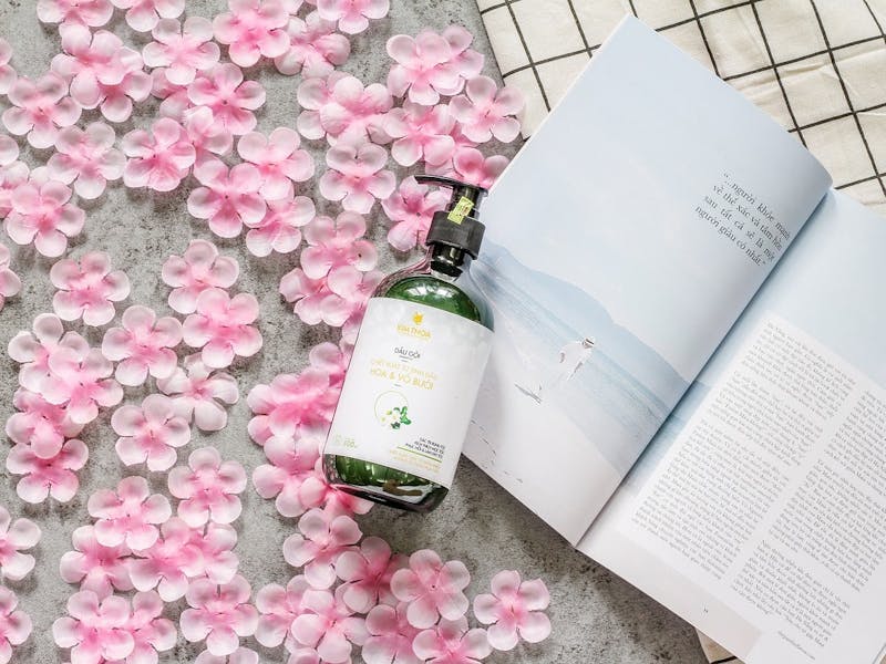 PerfectHair.ch_Shampoo Shampoo-Flasche neben einem Buch und vielen rosa Blüten auf dem Boden