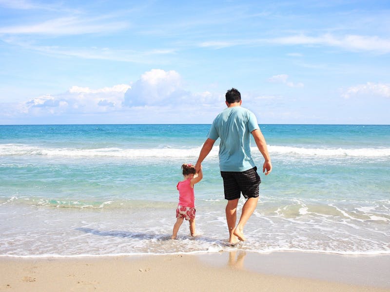 Ein Vater geht mit seiner Tochter am Strand spazieren.