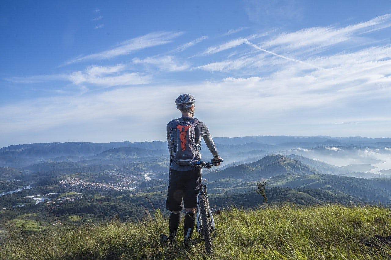 Hervis_Radfahren Radfahrer blickt vom Berg herab auf die Landschaft